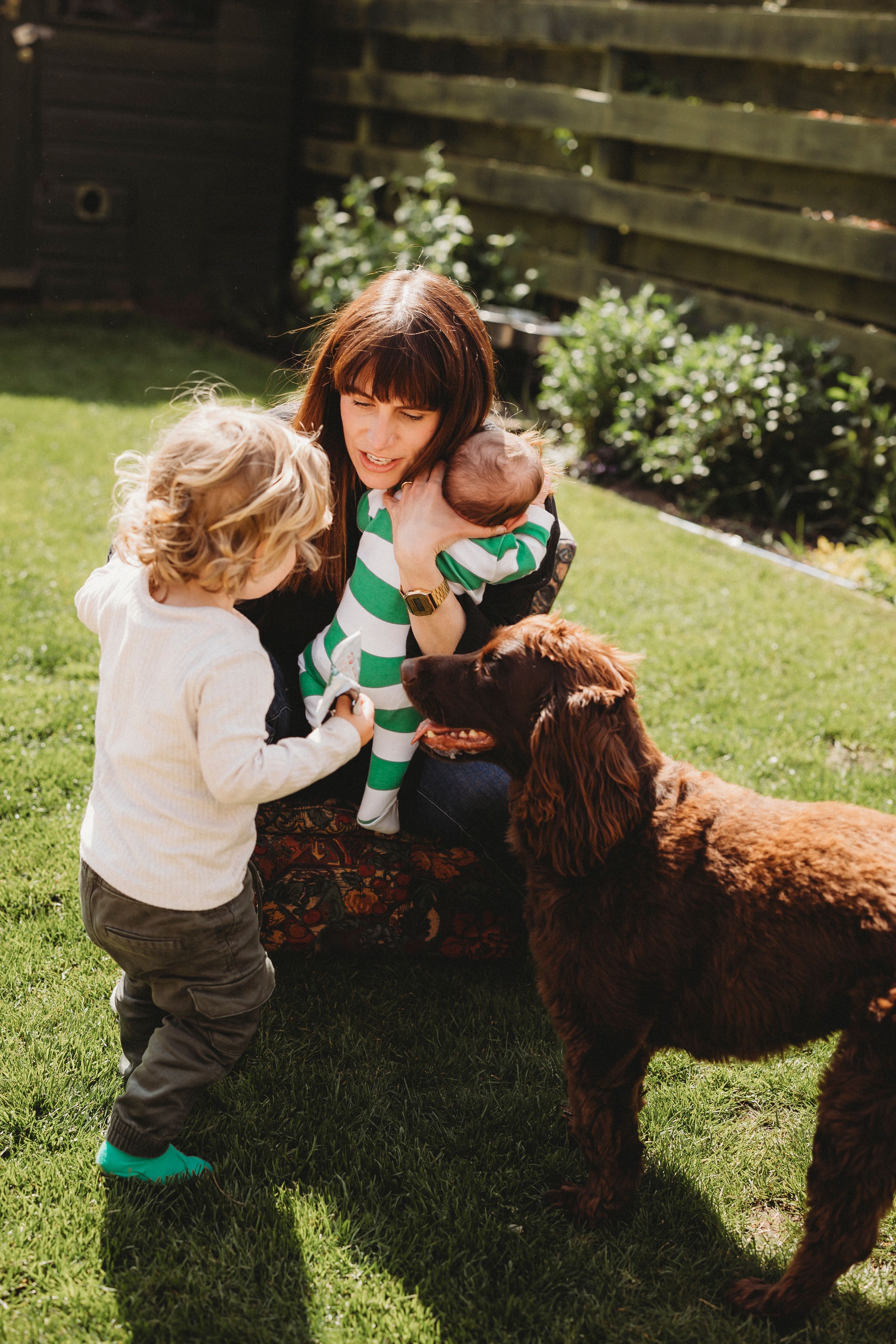 A joyful outdoor scene with children, adults and a brown dog in a sunny garden.