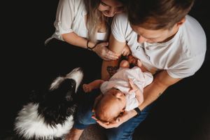 A couple tenderly holds their newborn baby while their Border Collie watches intently.