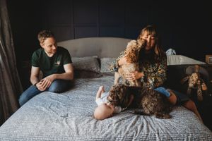 Family relaxing on bed with fluffy brown dog in dark room.