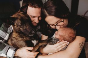 A family shares an intimate moment with their newborn baby and German Shepherd dog.
