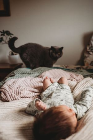 A grey cat watches over a sleeping baby on a pink knit blanket.