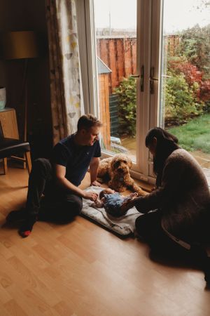A family sits by glass doors with their golden doodle and baby on a cushion.