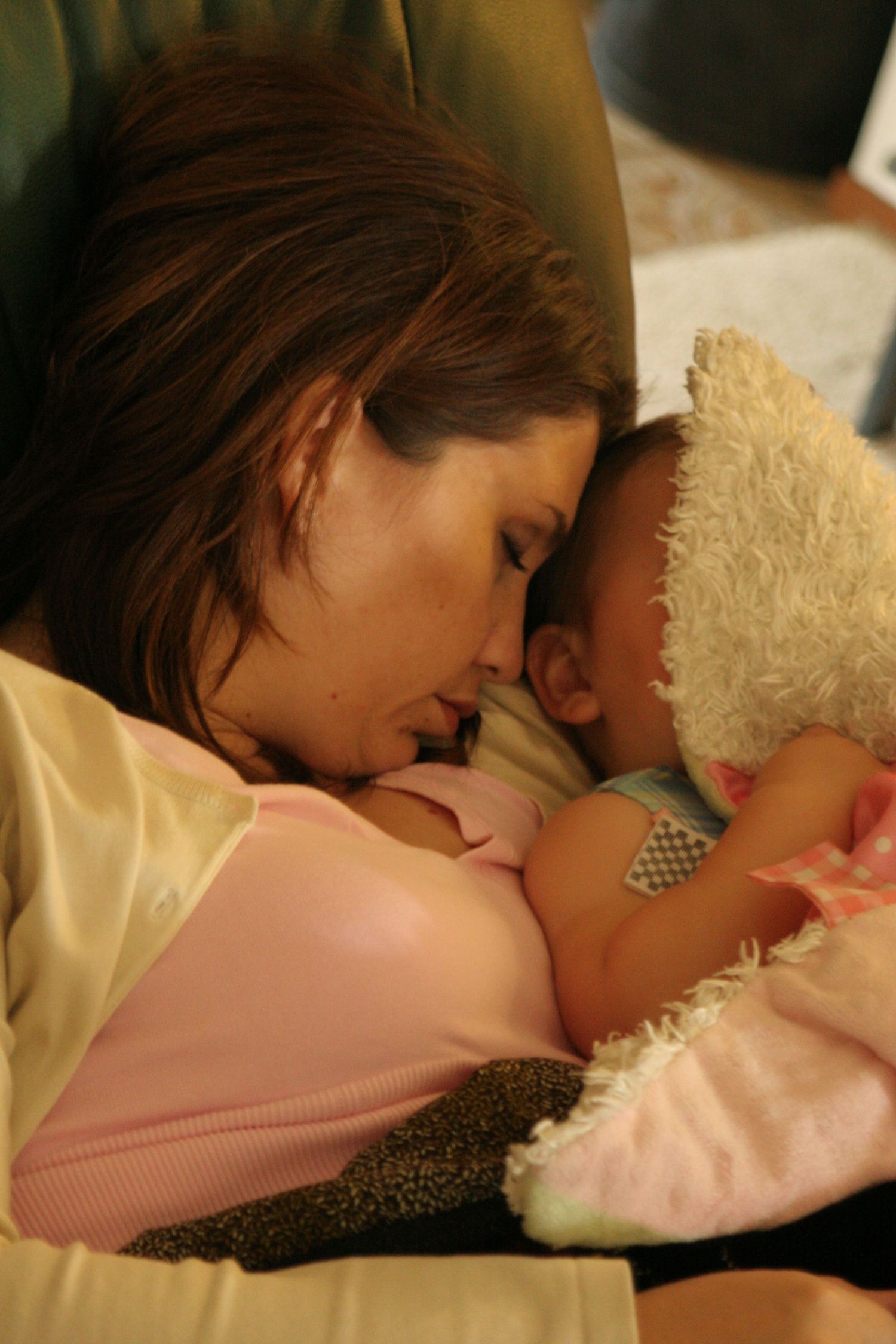 A mother tenderly holds her sleeping baby close, with a soft teddy bear nearby, in a warm and peaceful indoor setting.