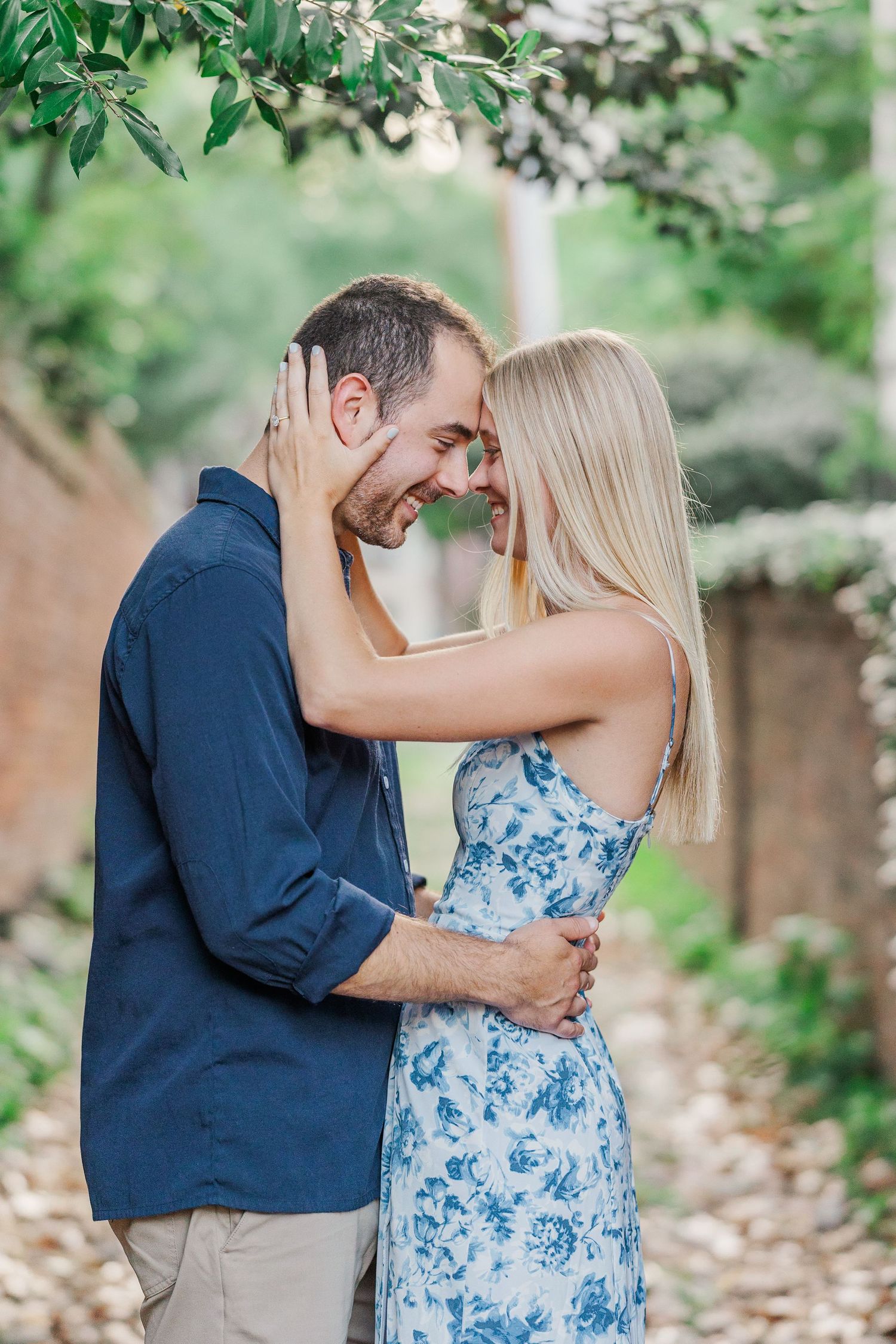 Couple embracing and almost kissing on a charming cobblestone alley lined with brick walls and lush greenery.
