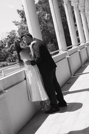 Black and white photo of a couple embracing and kissing on a columned outdoor terrace.