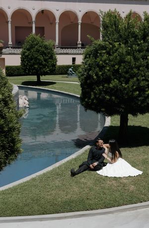 Bride and groom sitting together by a reflecting pool in a lush courtyard garden on their wedding day.
