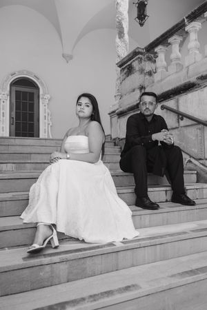 Bride and groom sitting apart on stone steps of elegant building in black and white wedding photo.