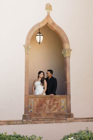 Couple posing romantically in an ornate Gothic stone archway with a lantern, woman in white dress, man in black suit.