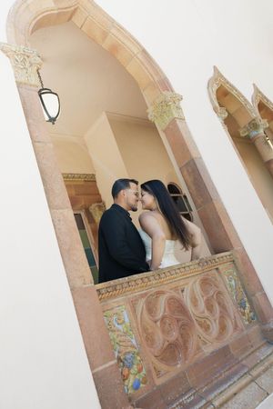 Bride and groom sharing romantic kiss on ornate balcony of historic building.