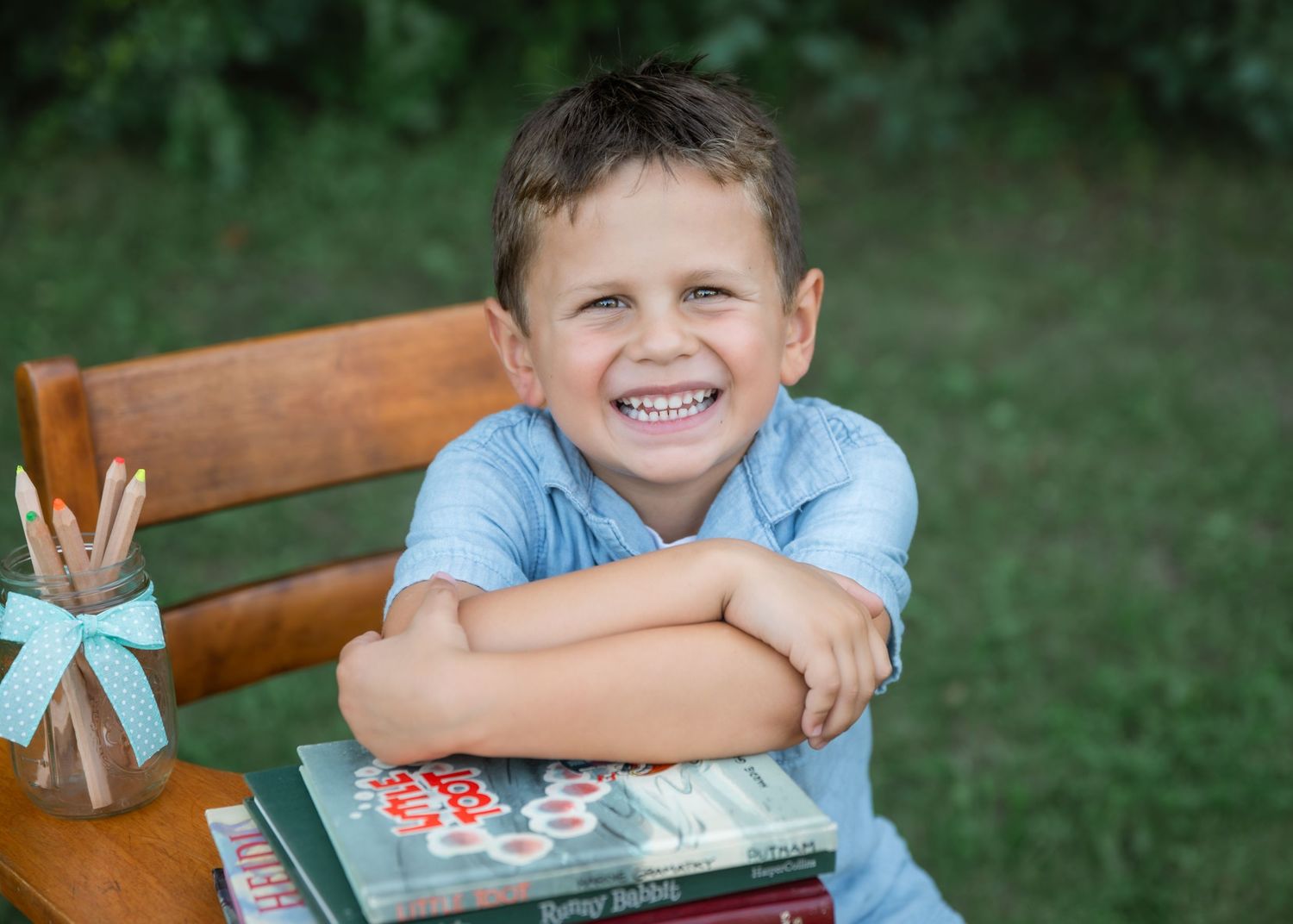 Happy young boy smiling at desk outdoors with stacked books and pencils, back to school photo.