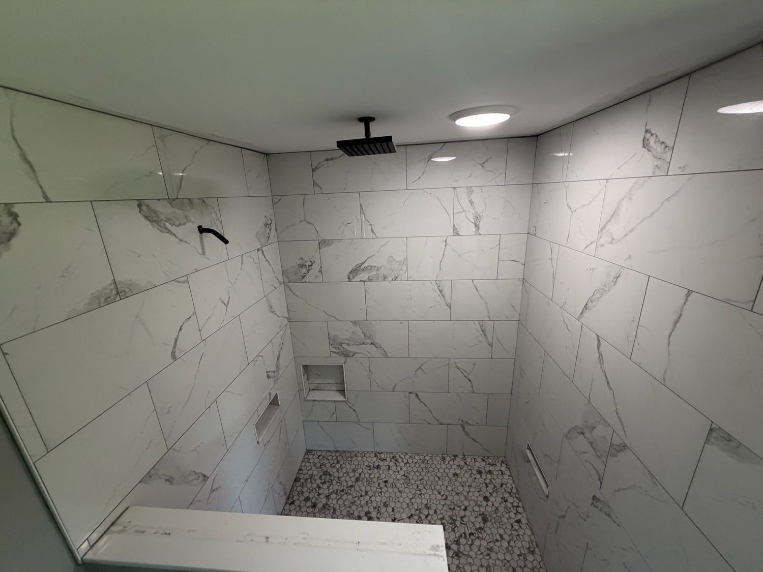 Luxury walk-in shower with large white marble tiles, pebble floor, built-in niche, and rain showerhead.