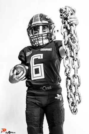 Black and white photo of a young football player in jersey number 6 holding a ball and large chain.