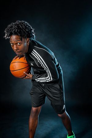 Young athlete in Adidas tracksuit dribbling basketball in dramatic dark studio with blue smoke.