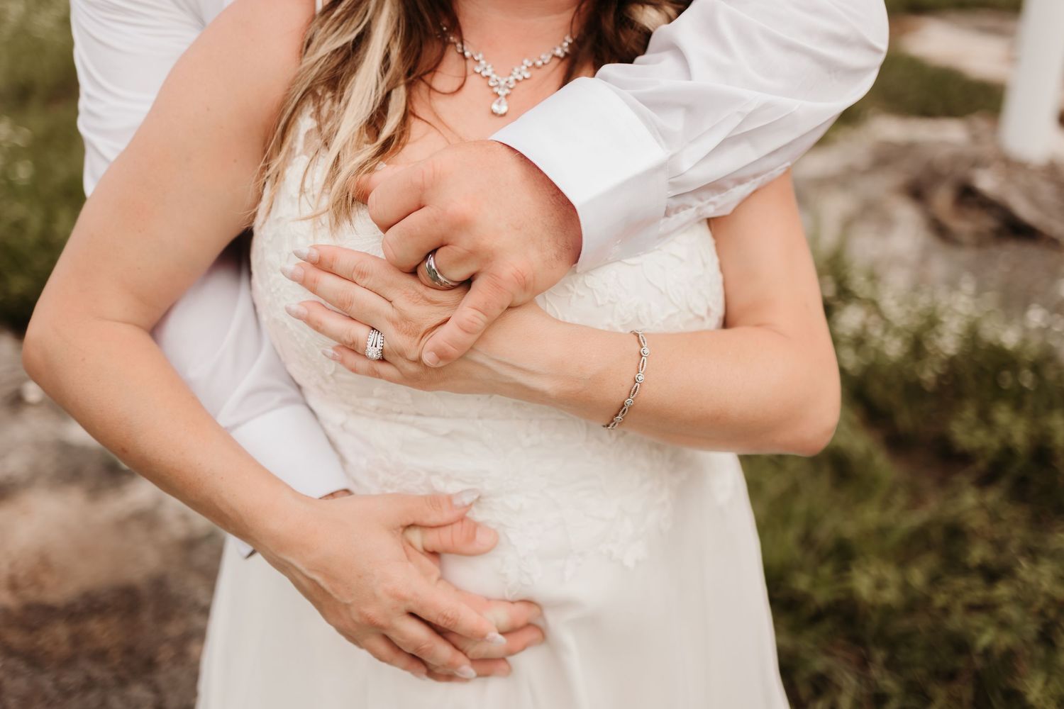 Close-up of bride and groom embracing, showcasing diamond engagement ring, bracelet, and elegant necklace on wedding day.