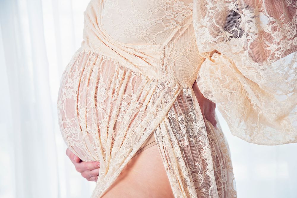 mother in lace cream dress holding pregnant belly