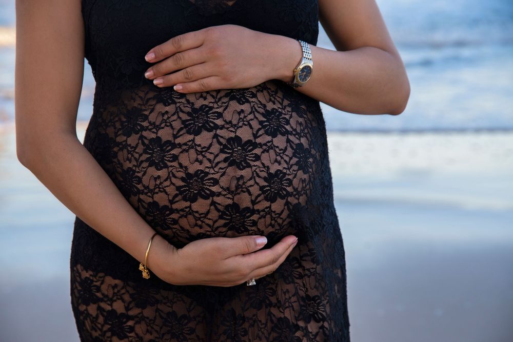 mother holding pregnant belly at the beach wearing a black lace dress
