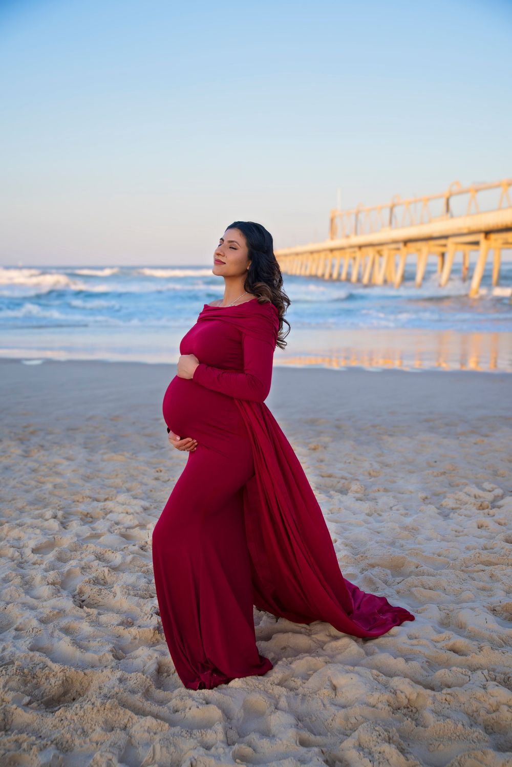 mother wearing a red flowing dress for her maternity session