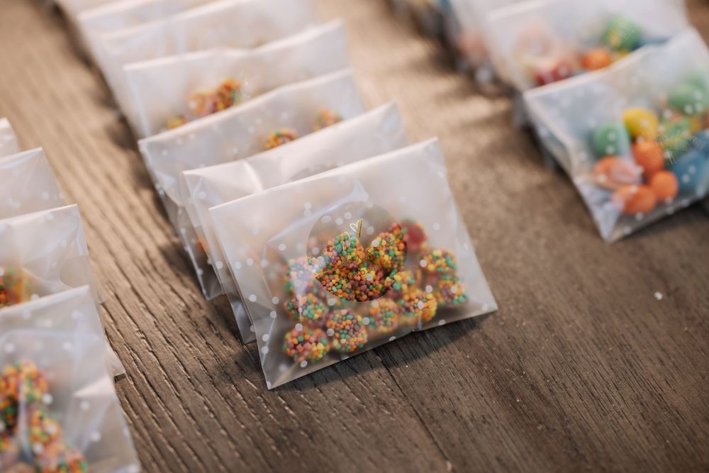 Small clear bags filled with colorful candy sprinkles arranged on a wooden table as party favors.