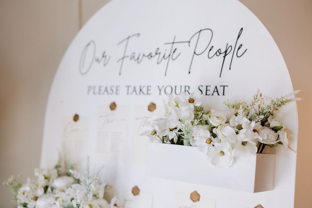 Elegant wedding seating chart sign reading Our Favorite People Please Take Your Seat with white floral arrangements.