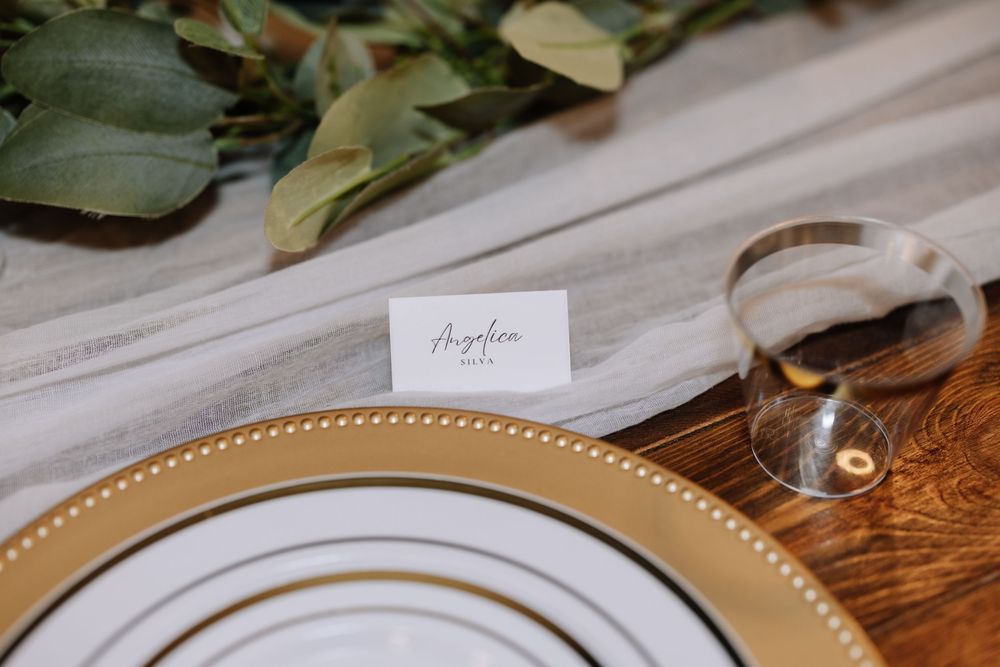 Elegant wedding place setting with gold charger plate, crystal glass, white place card, and eucalyptus greenery on linen runner.