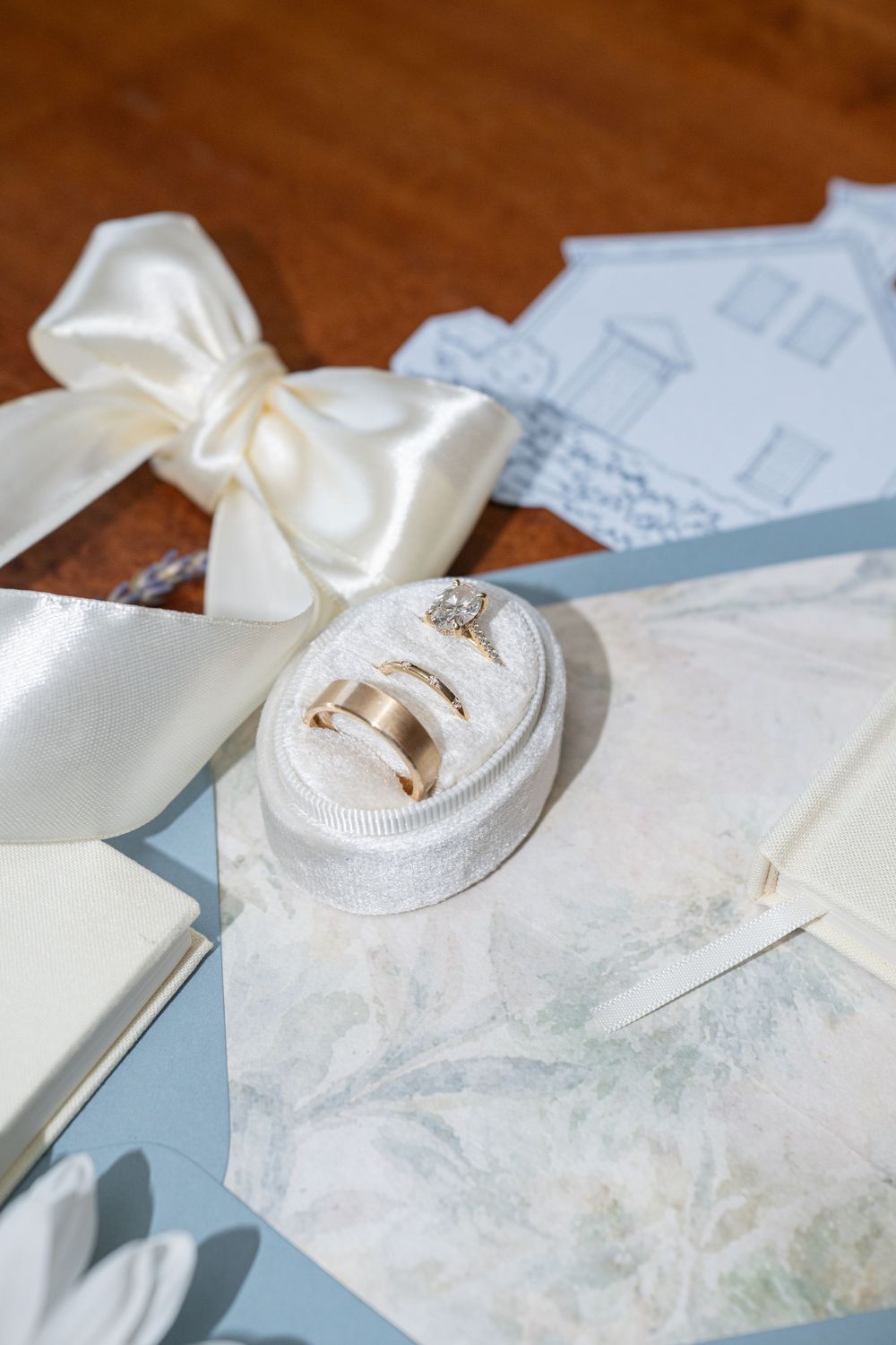 Gold wedding bands and diamond engagement ring in white velvet box with satin ribbon bow and elegant wedding stationery.