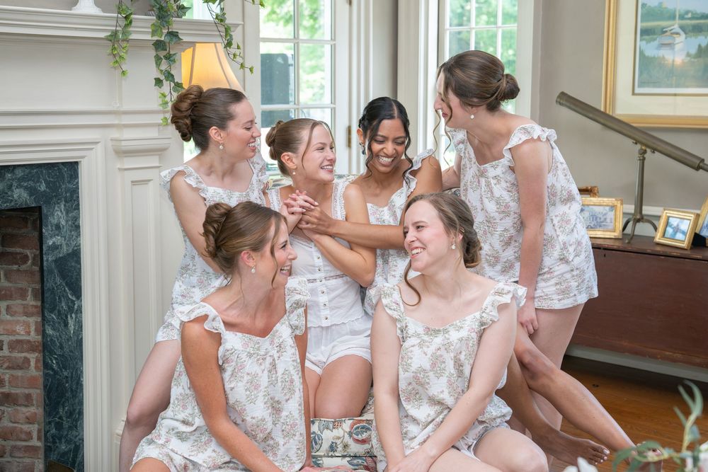 Bridesmaids in matching floral rompers laughing and celebrating together in an elegant room before a wedding.
