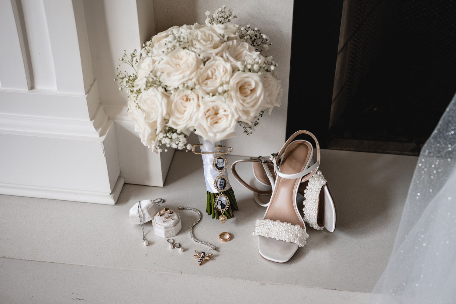 White bridal bouquet of roses with pearl-adorned heels, delicate jewelry, and lace veil arranged on white surface.
