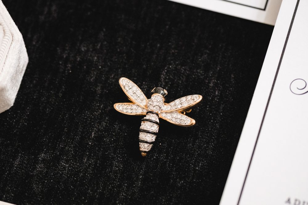 Rose gold dragonfly brooch with sparkling crystal pavé details displayed on black velvet surface.