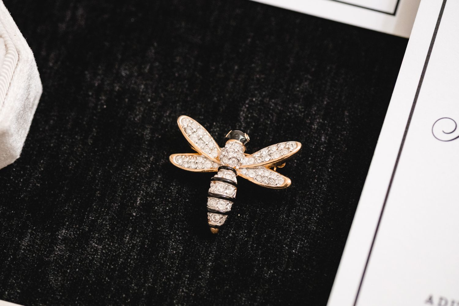 Rose gold dragonfly brooch with sparkling crystal pavé details displayed on black velvet surface.