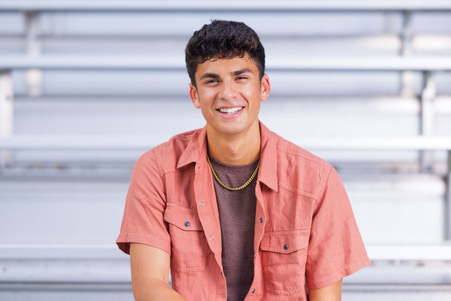 Young man in red shirt and jeans posing on a wooden suspension bridge surrounded by lush green trees.