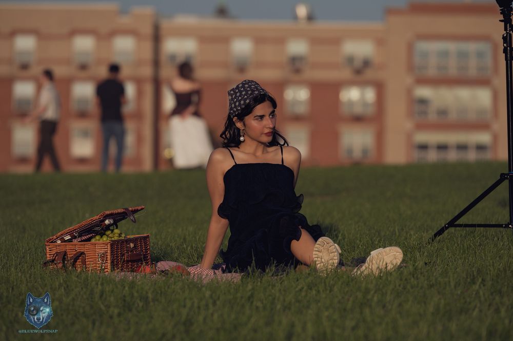 Young woman in black dress and patterned headscarf sitting on green grass with a vintage picnic basket. Chi.Shooters meet itsaqsaforyou