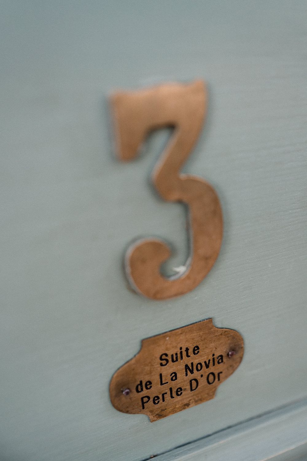 Brass number three and Suite de La Novia Perle D'Or plaque on a mint green door.