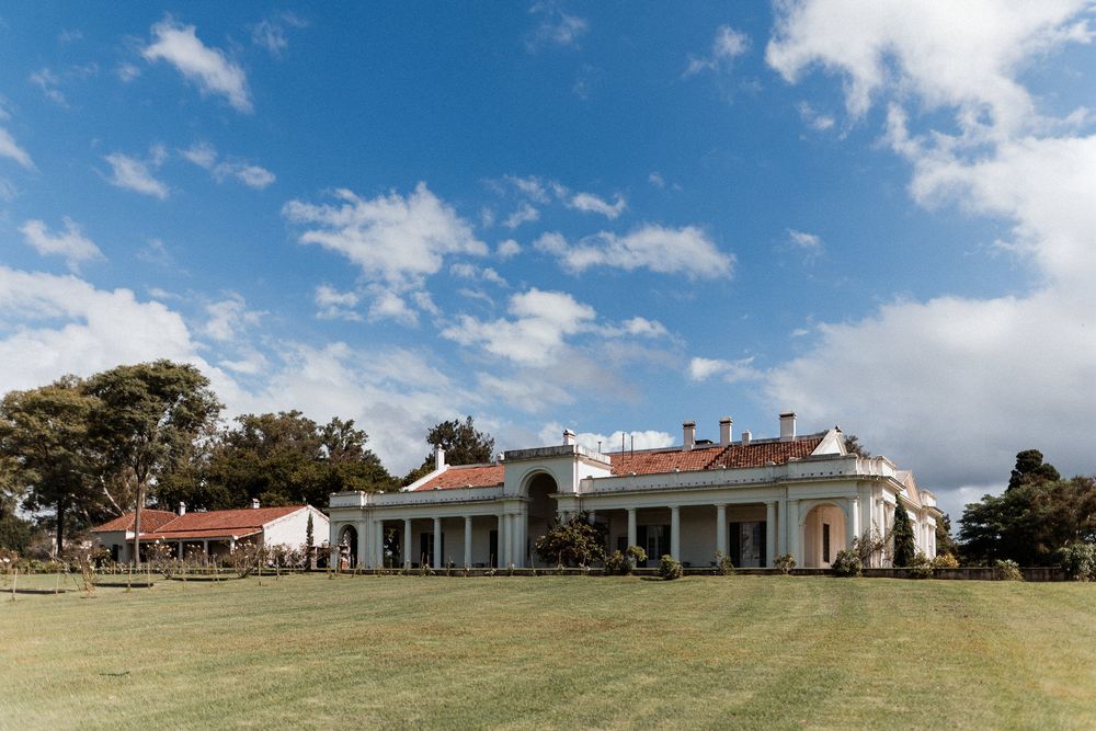 Elegant white colonial mansion with red tile roof surrounded by green lawns under a blue sky.