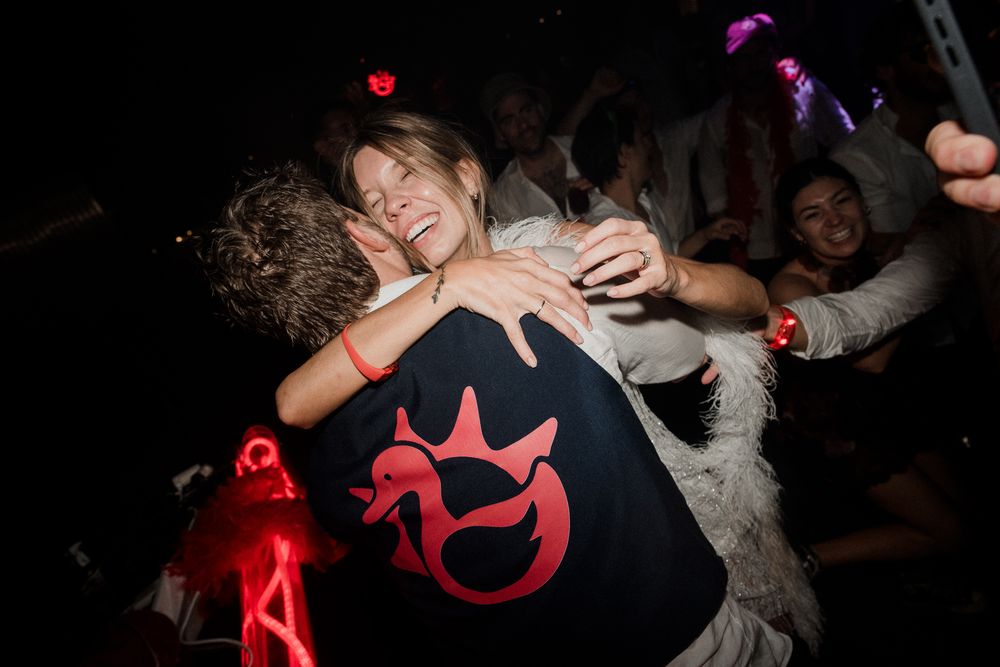 Two people hugging and dancing at a lively nightclub party with colorful lights in the background.