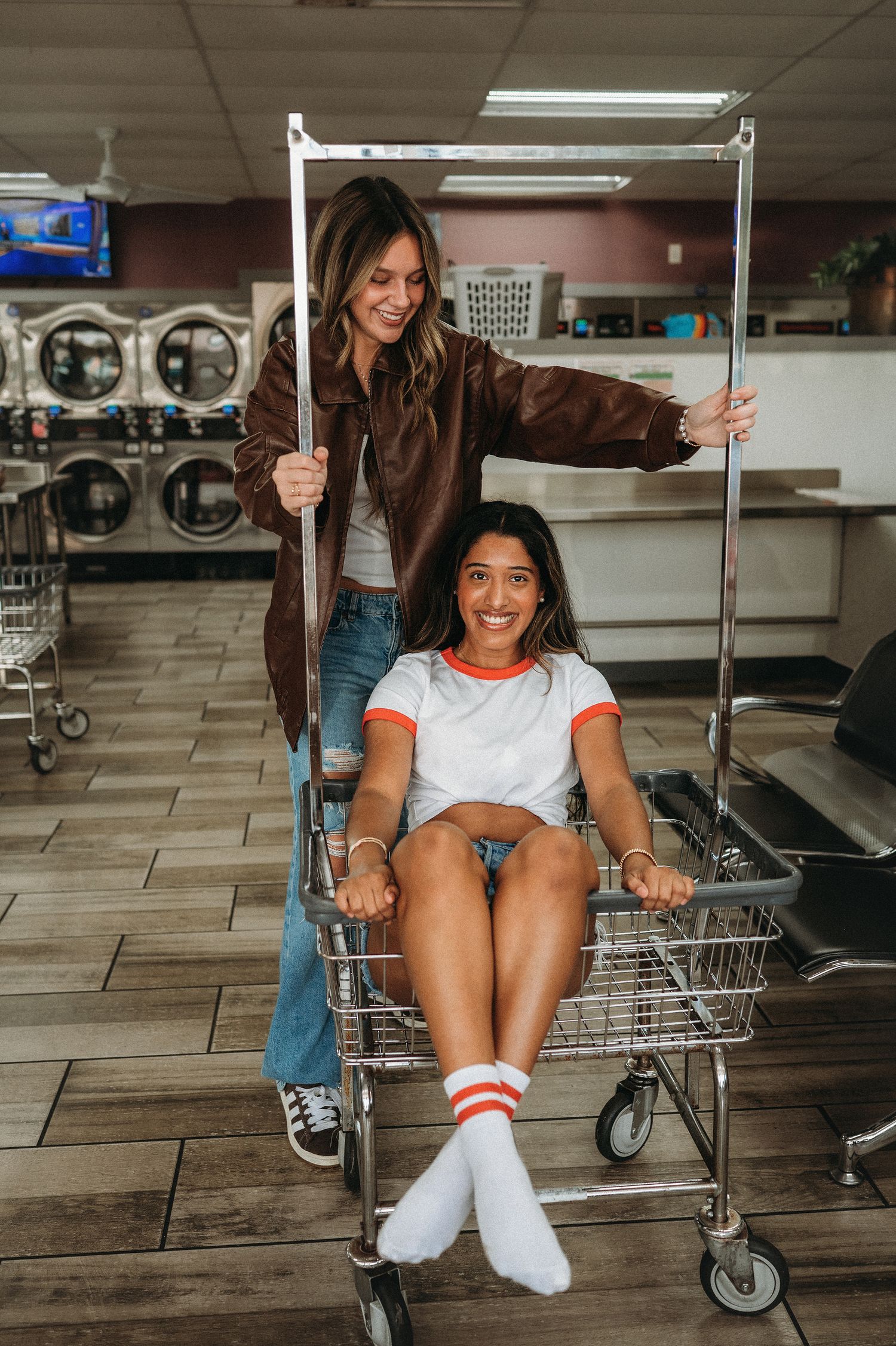 2 girls in a laundromat playing in a cart