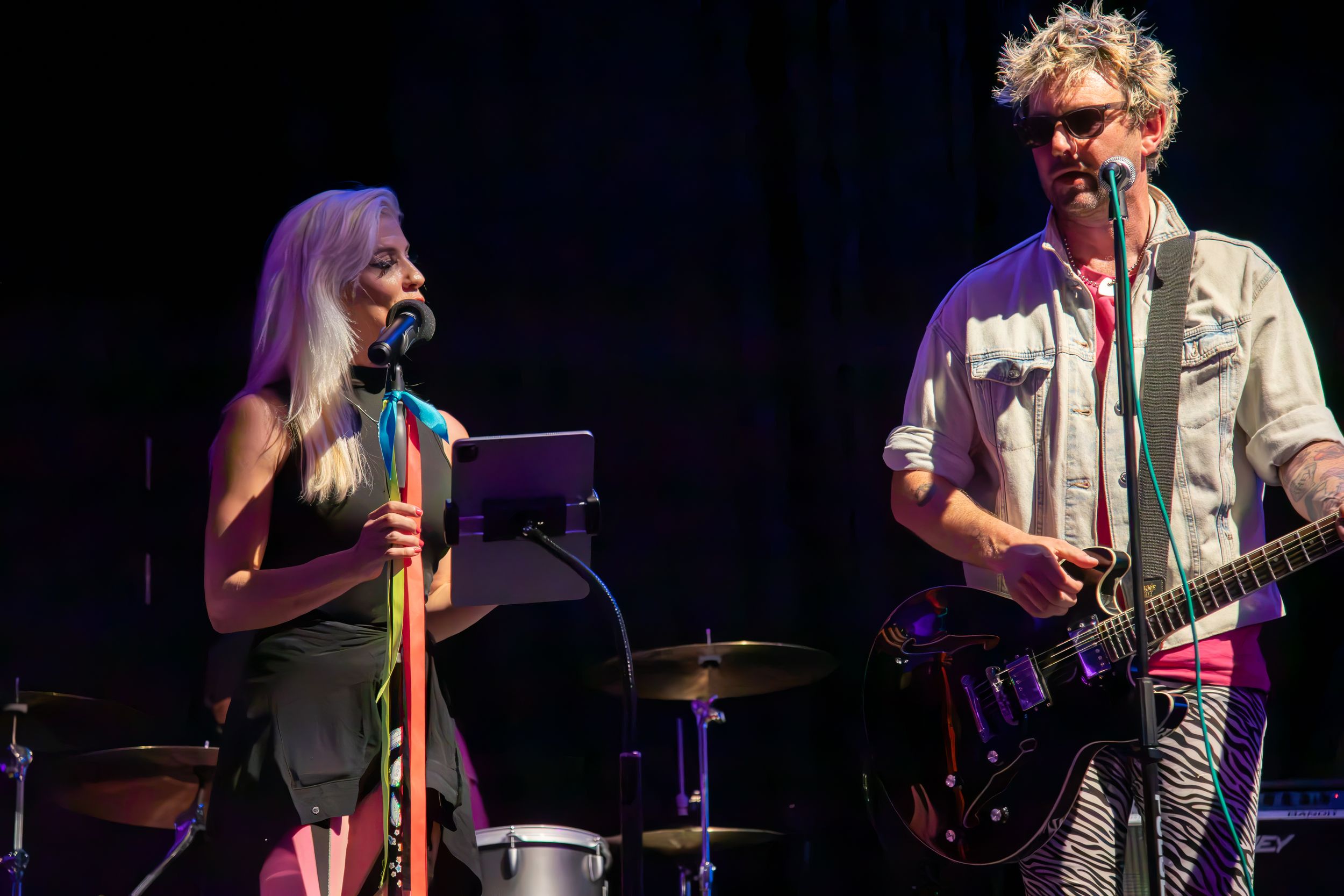 Blonde female vocalist and male guitarist performing together on a lit stage.