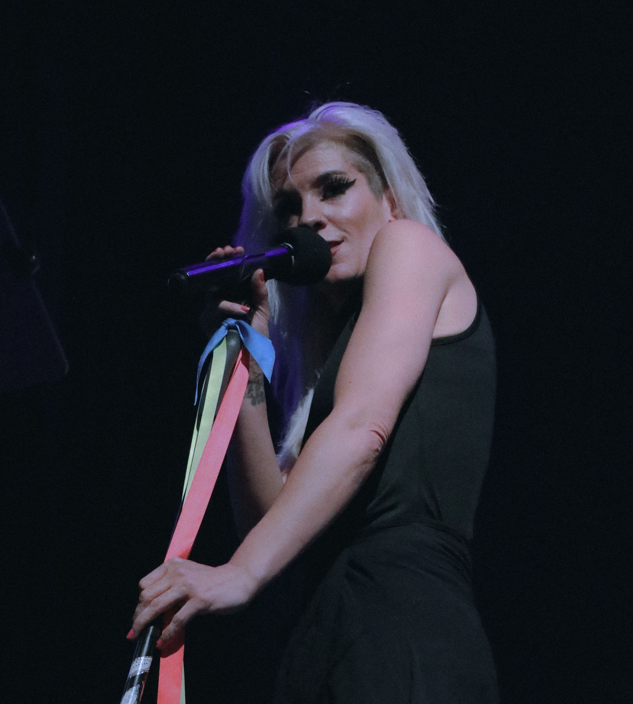 Blonde female singer in black dress performing on stage holding colorful ribbon streamers.