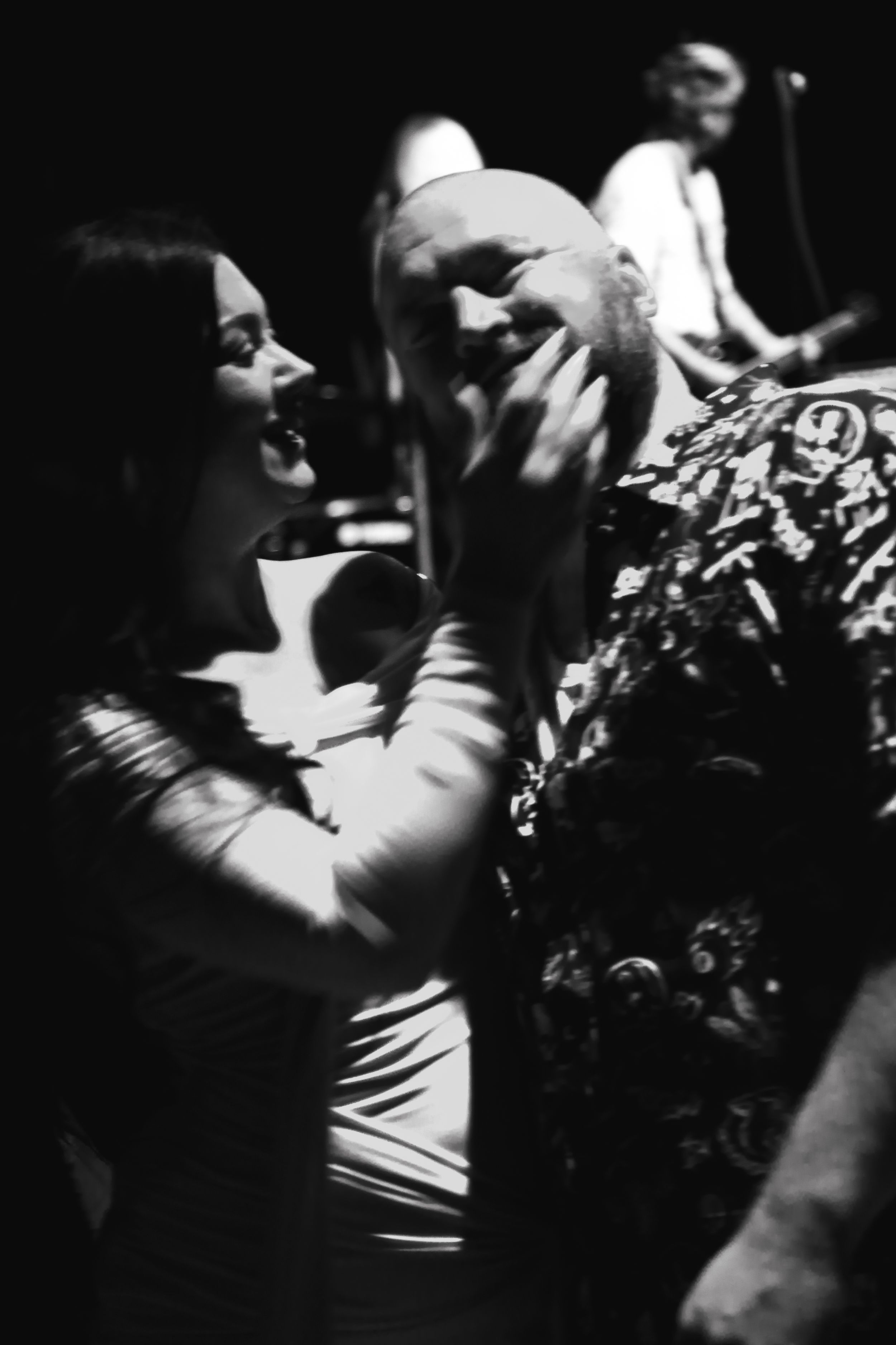 Black and white photo of a woman and bearded man sharing an intimate moment at a concert.