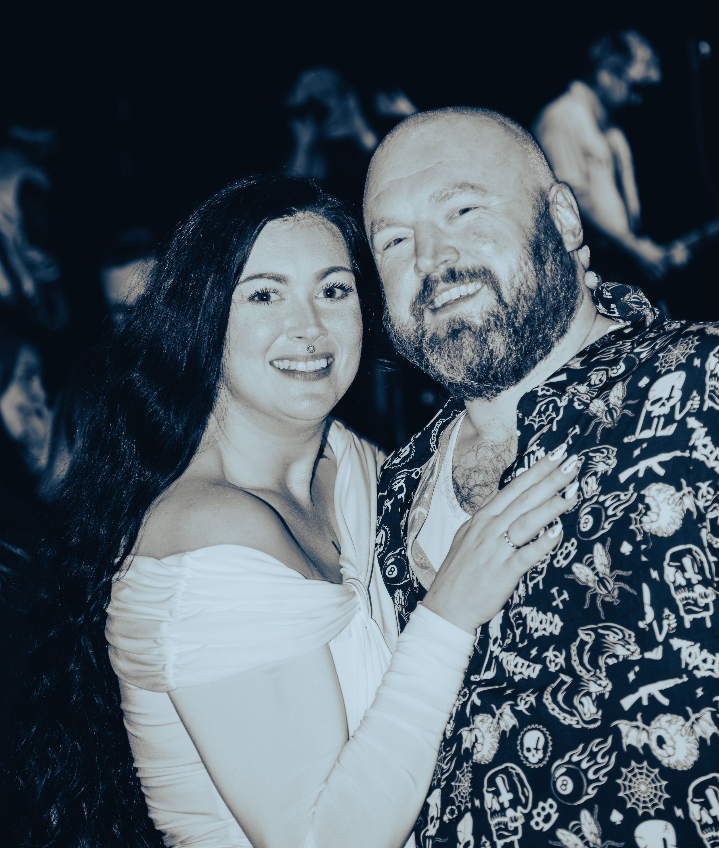 Smiling woman in white dress posing with bearded man in patterned shirt at an event.