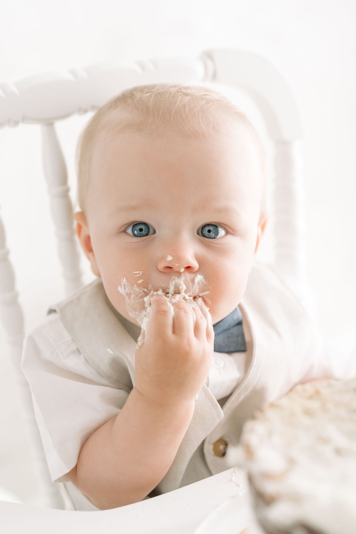 Portrait de Bébé aux grands yeux bleus qui regarde la caméra, une main pleine de crémage blanc dans la bouche