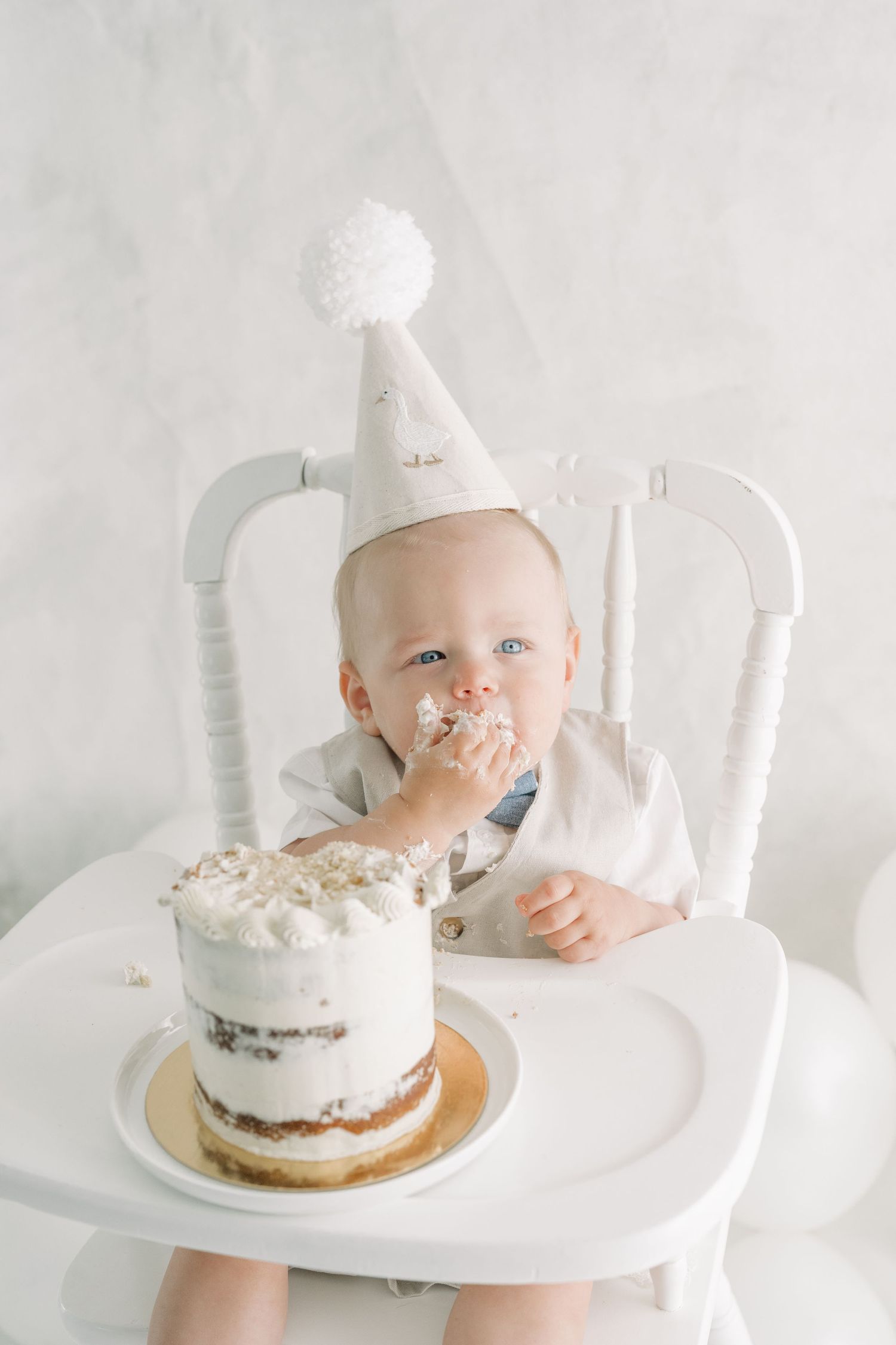 Bébé portant un chapeau de lin beige à pompon blanc découvrant son gâteau d'anniversaire avec ses mains dans le crémage