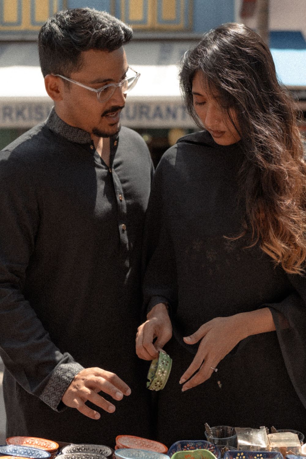 Couple in black outfits browsing colorful ceramic plates at an outdoor market stall.