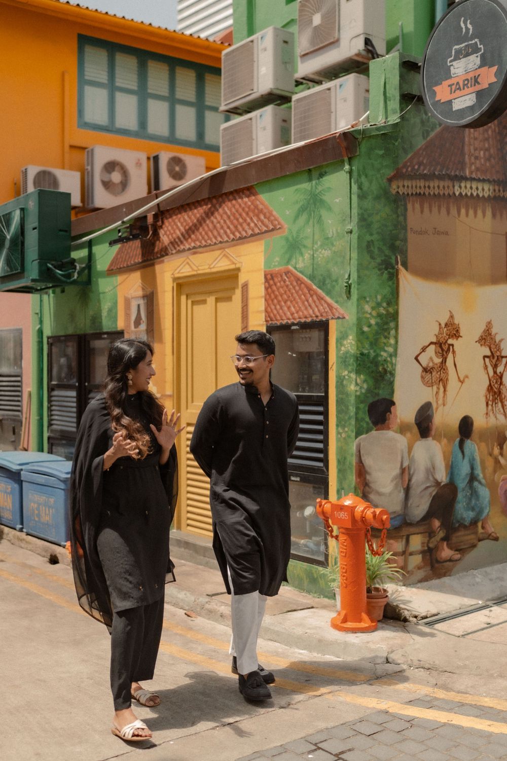Two people in black traditional attire walk past a colorful street mural in a vibrant urban setting.