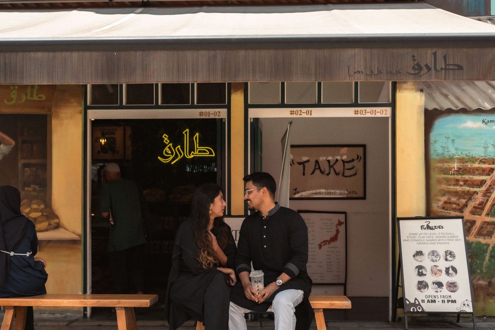 Couple sitting together outside a restaurant with Arabic signage and a TAKE sign in an urban setting.