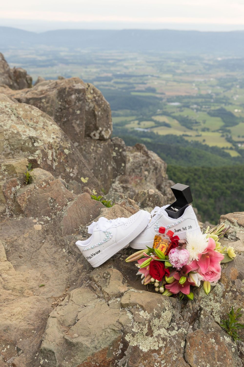 White wedding sneakers and bridal bouquet on rocky mountain summit with scenic valley views below.