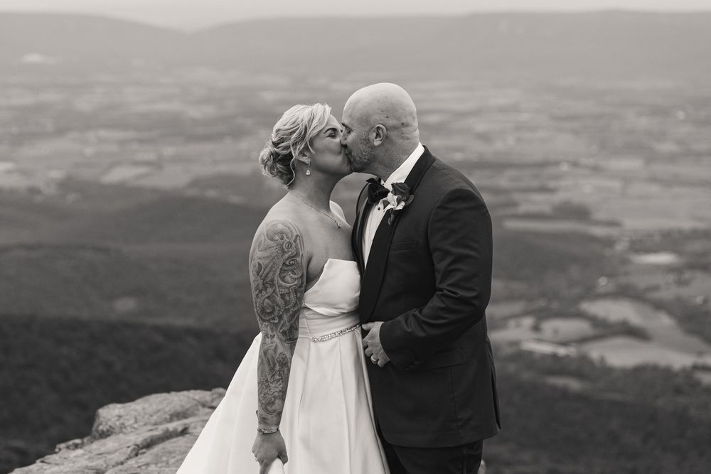 Bride and groom share a romantic kiss on a mountain overlook in a stunning black and white wedding photo.