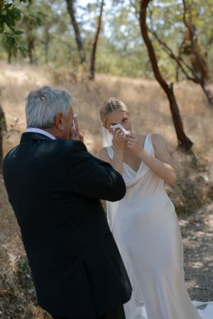 A couple in formal attire dances together in a natural outdoor setting with trees in the background.