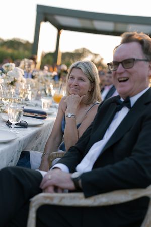 Guests seated at an elegant outdoor wedding reception with formal place settings and glassware at sunset.