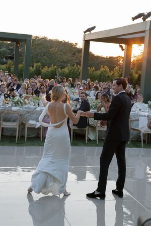 A wedding couple dances together during their first dance on an outdoor dance floor at sunset.