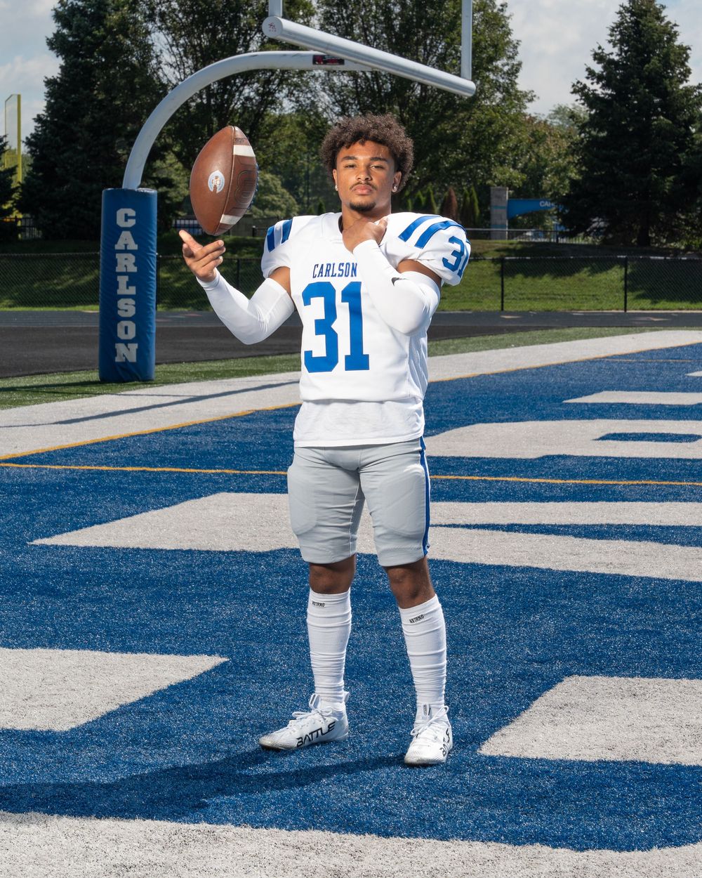 Carlson #31 football player in white and blue uniform tossing a football on a blue turf field.